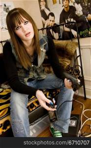 Teenage girl sitting on a bed and holding a mobile phone and a video game