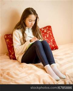 Teenage girl sitting on bed and writing poems in notebook