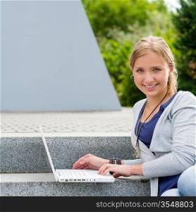 Teenage girl sitting on steps with laptop happy smiling student