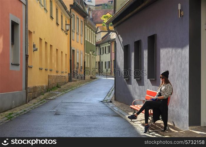 Teenage girl sitting on the bench on old city street Bamberg, Germany