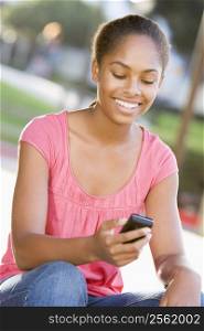 Teenage Girl Sitting Outdoors Using Mobile Phone