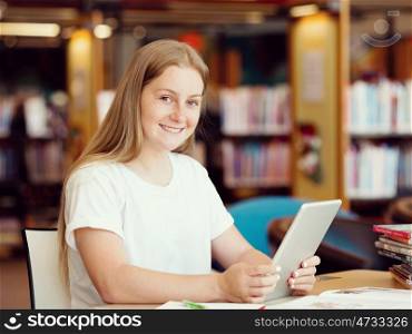 Teenage girl sitting with tablet in library. Teenage girl with tablet in library