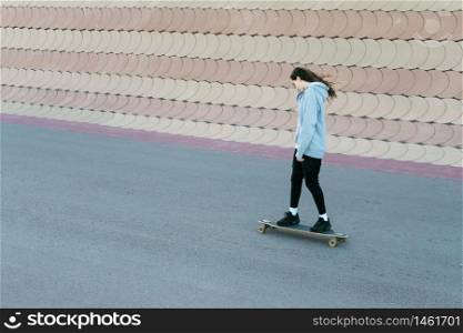 Teenage girl skating on a longboard in a city park in a sunny day