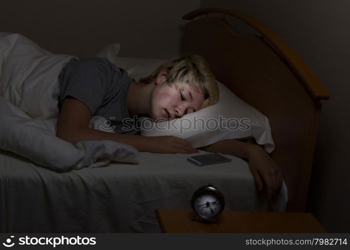 Teenage girl sleeping bed with her cell phone on night stand. Teen surrounded by technology even late at night.
