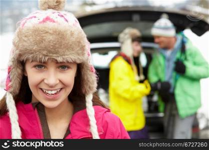 Teenage Girl Smiling At Camera Whilst Family Load Skis In Boot Of Car