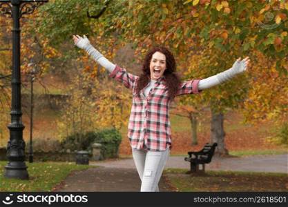 Teenage Girl Standing In Autumn Park With Arms Outstretched