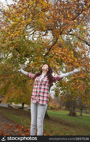 Teenage Girl Standing In Autumn Park With Arms Outstretched