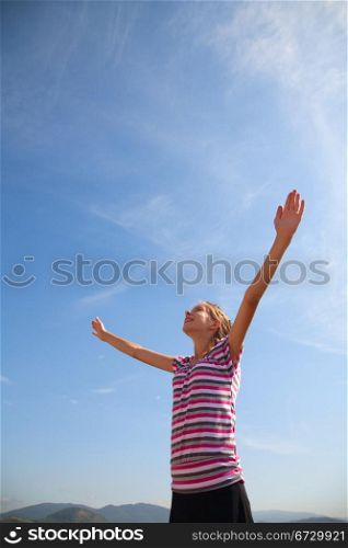 Teenage girl staying with raised hands against blue sky