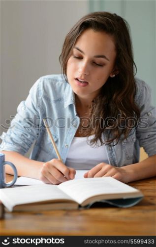 Teenage girl studying book at home writing notes concentrating