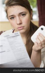 Teenage Girl Studying Mobile Phone Bill Looking Worried