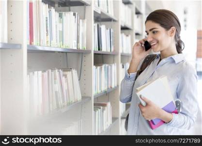 Teenage girl talking on smartphone while standing in library