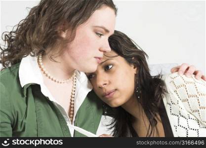 Teenage girl trying to comfort her friend who has just found out she is pregnant, still holding the pregnancy stick