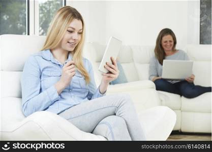 Teenage Girl Uses Digital Tablet Whilst Mother Works On Laptop