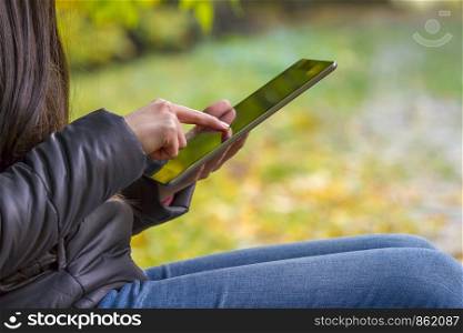Teenage girl using digital tablet computer in autumn park closeup