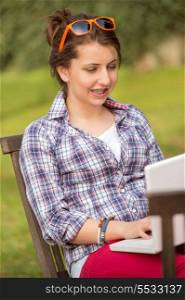 Teenage girl using laptop sitting on bench at park