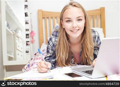 Teenage Girl Using Laptop To Do Homework In Bedroom