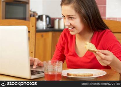 Teenage Girl Using Laptop Whilst Eating Breakfast