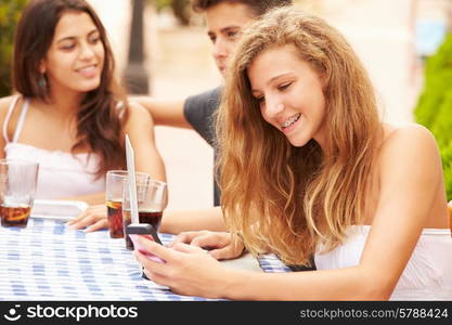 Teenage Girl Using Mobile Phone Sitting At Caf? With Friends