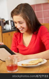 Teenage Girl Using Tablet Computer Whilst Eating Breakfast