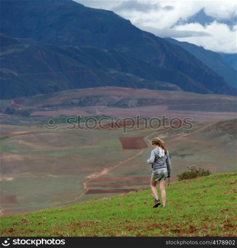 Teenage girl walking in a field with Sacred Valley in the background, Cusco Region, Peru