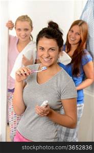 Teenage girl washing her teeth with friends in the bathroom
