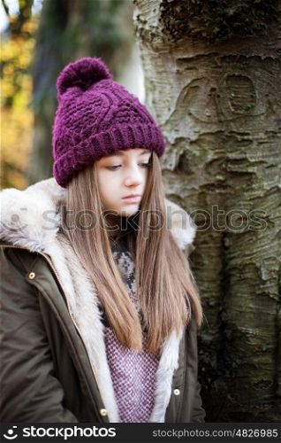 Teenage girl wearing a woolen hat standing beside a tree