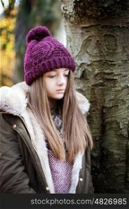 Teenage girl wearing a woolen hat standing beside a tree