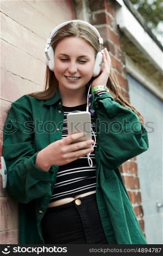 Teenage Girl Wearing Headphones And Listening To Music In Urban Setting