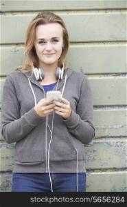 Teenage Girl Wearing Headphones And Listening To Music In Urban Setting