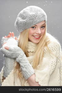 Teenage Girl Wearing Warm Winter Clothes And Hat Holding Snowball In Studio