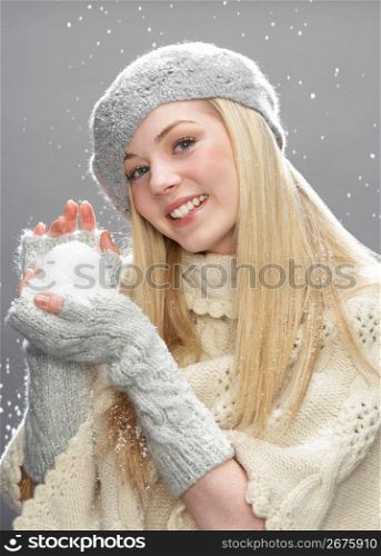 Teenage Girl Wearing Warm Winter Clothes And Hat Holding Snowball In Studio