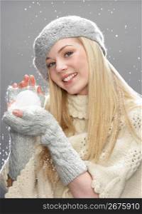 Teenage Girl Wearing Warm Winter Clothes And Hat Holding Snowball In Studio
