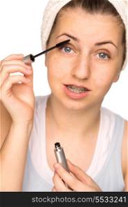 Teenage girl with braces applying mascara on white background