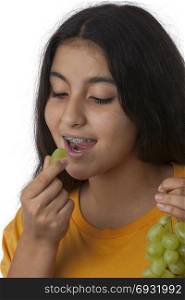 Teenage girl with dental braces eating healthy green grapes grapes