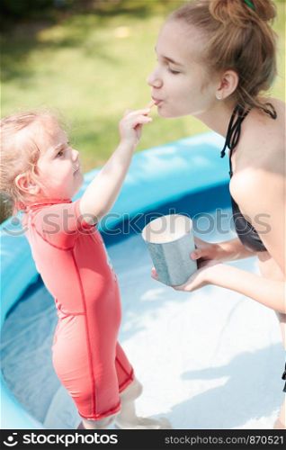 Teenage girl with her little sister spending time in the swimming pool enjoy eating ice cream on a summer day