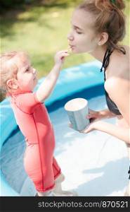 Teenage girl with her little sister spending time in the swimming pool enjoy eating ice cream on a summer day