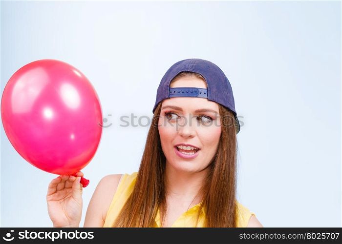 Teenage girl with red balloon.. Teenage girl making funny silly faces. Young trendy woman in jeans cap holding red balloon.