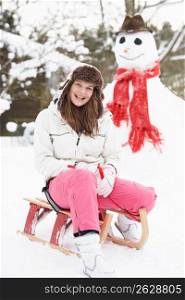 Teenage Girl With Sledge Next To Snowman