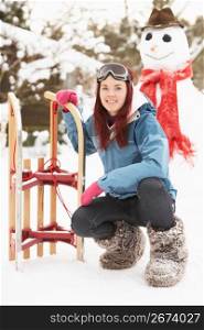 Teenage Girl With Sledge Next To Snowman
