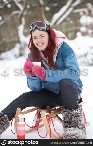 Teenage Girl With Sledge Next To Snowman With Flask And Hot Drink