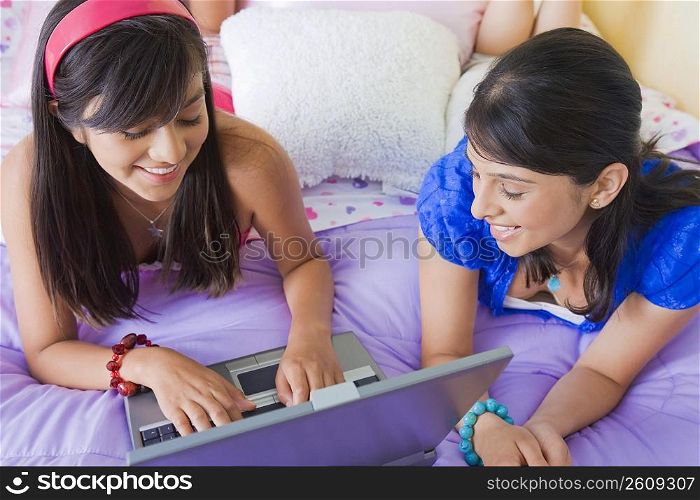 Teenage girl working on a laptop with a young woman lying beside her on the bed