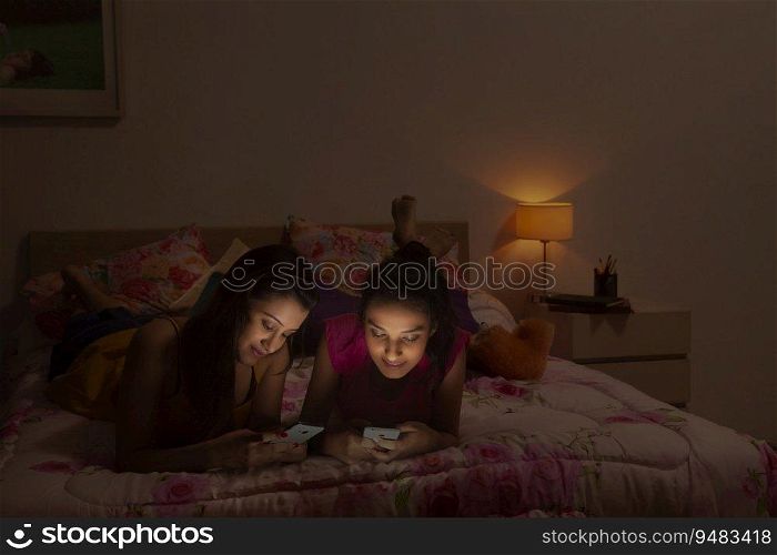 Teenage girls lying on the bed and texting on their mobile phones. 
