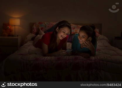 Teenage girls lying on the bed using their mobile phones and smiling. 