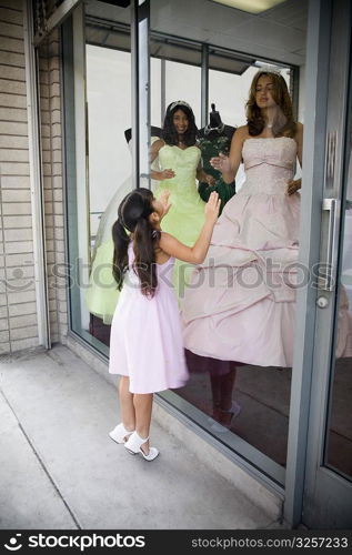 Teenage girls posing as mannequins in dress shop window as young girl looks dreamily into store