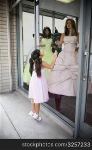 Teenage girls posing as mannequins in dress shop window as young girl looks dreamily into store