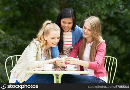 Teenage Girls Sitting At Outdoor cafeWith Mobile Phone