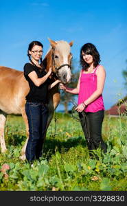 Teenage girls standing on a meadow in summer with their horse