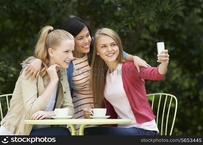 Teenage Girls Taking Photo On Mobile Phone At Outdoor cafe