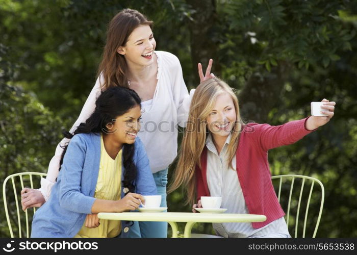 Teenage Girls Taking Photo On Mobile Phone At Outdoor cafe