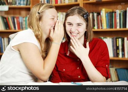 Teenage girls telling secrets in school library.